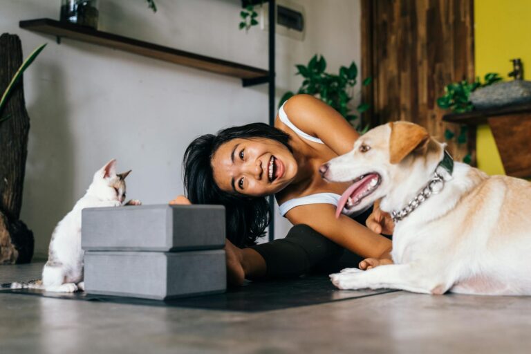 Smiling woman practicing yoga indoors with her dog and cat, embracing a healthy lifestyle. (Photo by Anna Tarazevich on Pexels)